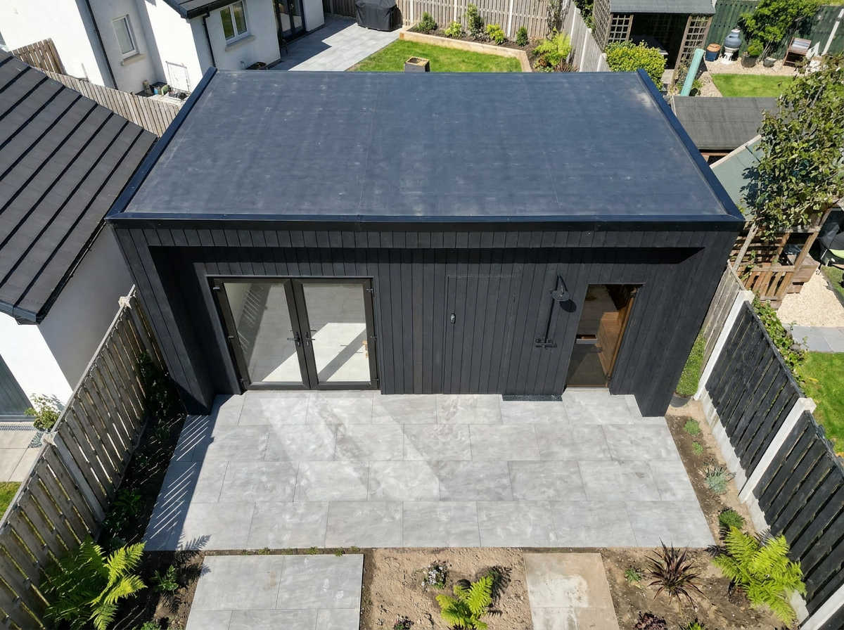 Aerial view of black-clad garden room with flat roof and grey porcelain patio